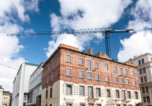 old brick building under reconstruction with building crane on blue sky background